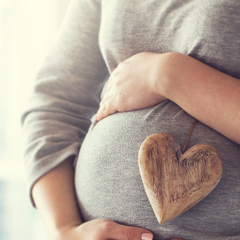 Young pregnant woman holds wooden heart. Love concept. Pastel toning
